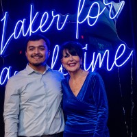 Boy in button up and President Mantella stand in front of Laker for a Lifetime neon sign